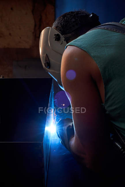 Vue latérale de l'artisan en masque protecteur portant des combinaisons et des gants travaillant en atelier et soudant la construction métallique — Photo de stock