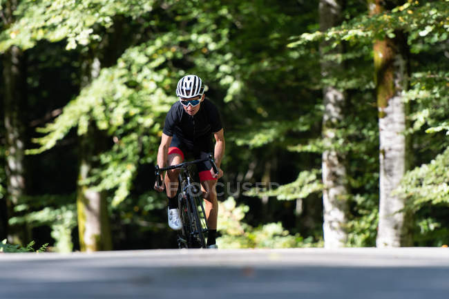 Sportsman in protective helmet and goggles riding bicycle along path during race on sunny day in park — Stock Photo
