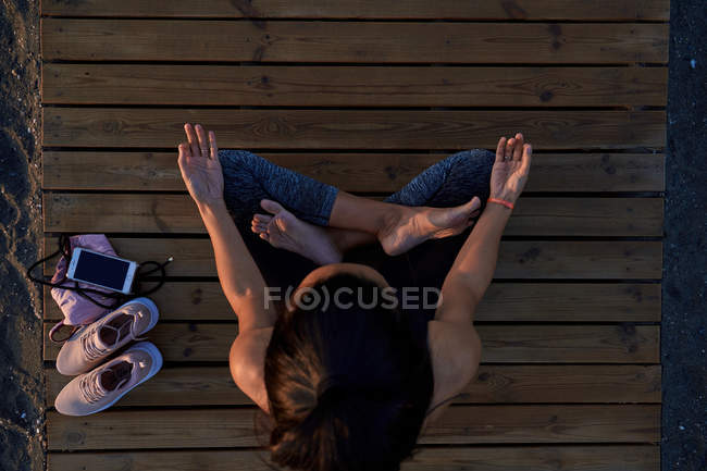 From Above Barefoot Female In Sportswear Sitting In Lotus Pose On Lumber Path And Meditating During Yoga Training Closed Eyes Crossed Legs Stock Photo