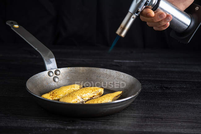 Male chef melts cheese on a platter with a burner — Stock Photo