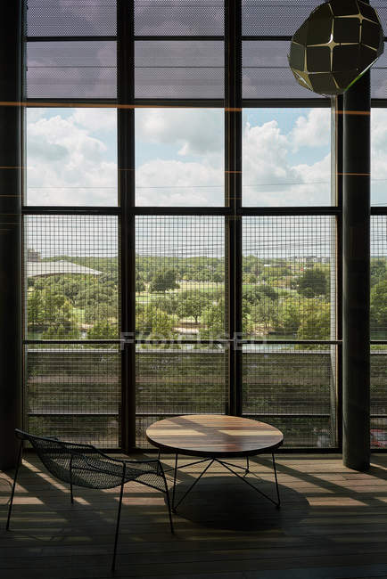 Zona salotto con tavolo rotondo in legno e sedia in metallo contro alte finestre con griglia in contrasto di luce in libreria Texas — Foto stock