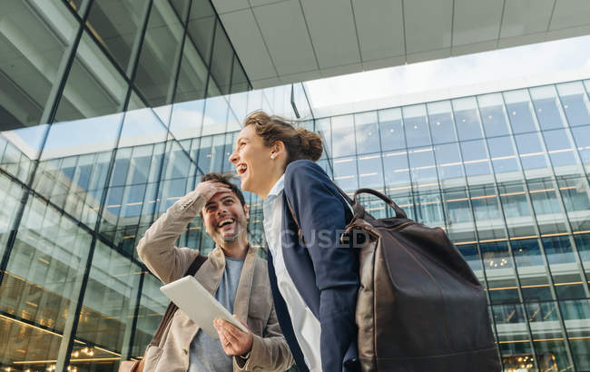 Optimistic business people smiling and browsing on tablet while standing outside modern building and resting after work — Stock Photo