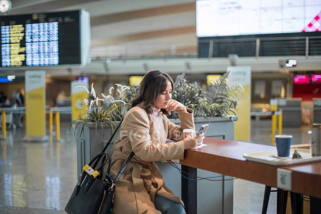 Frau sitzt am Flughafen und nutzt Smartphone — Stockfoto