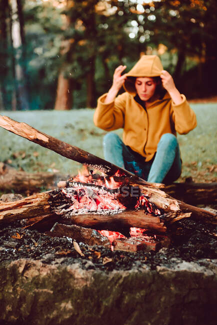 Mulher viajante aquecendo as mãos perto de fogueira na clareira da floresta — Fotografia de Stock