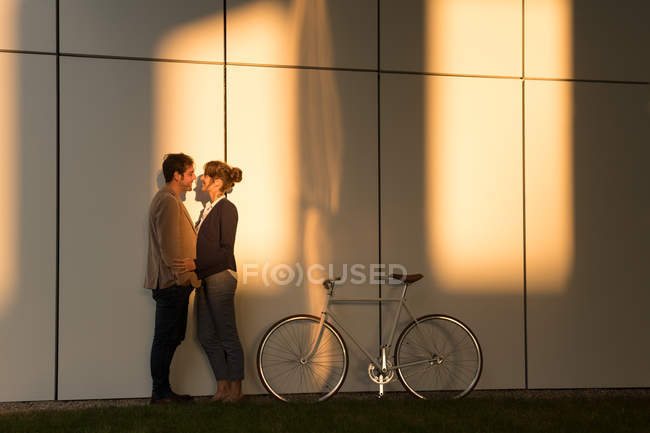 Businessman embracing girlfriend while standing near bicycle outside modern building after work — Stock Photo