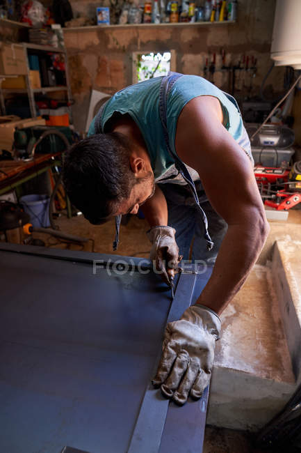 Middle aged craftsman in protective gloves marking metal sheet while working in workshop — Stock Photo