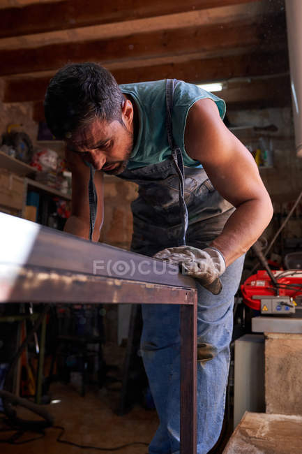 Middle aged craftsman in protective gloves marking metal sheet while working in workshop — Stock Photo