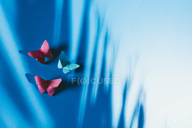 Papillons fragiles en papier attachés au tissu de soie bleue avec ombre de palmier — Photo de stock