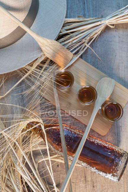 Whiskey shots on wooden board with hat, wooden tableware and wheat on rustic table — Stock Photo