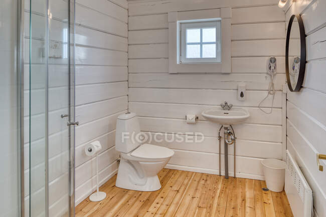 Elegante interior do banheiro minimalista com piso de madeira e paredes brancas com pequena janela em casa — Fotografia de Stock