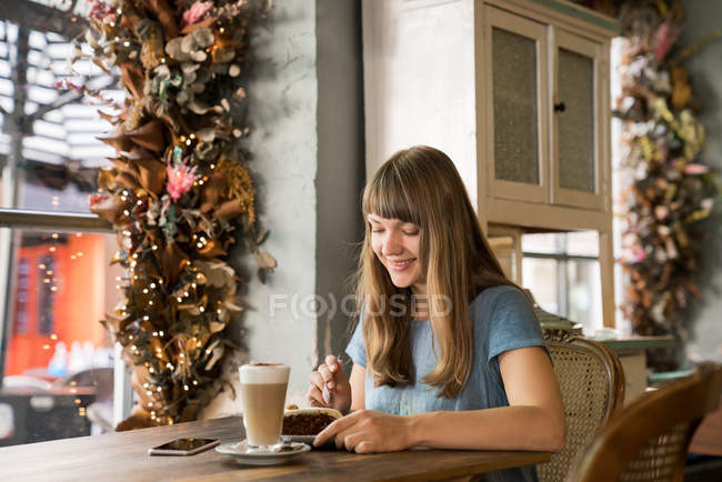 Bionda felice giovane femmina con frangia sorridente e mangiare dessert in accogliente caffè — Foto stock