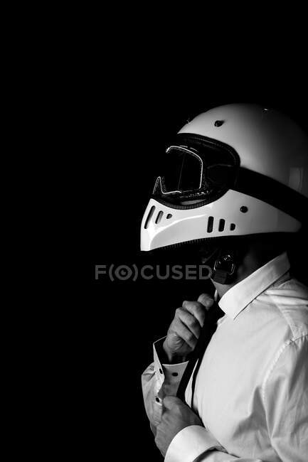 Стильный водитель в шлеме и очках, регулирующий галстук в студии — стоковое фото