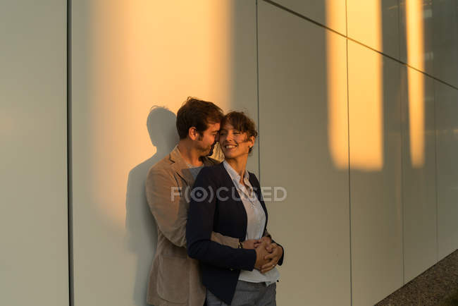 Businessman embracing girlfriend while standing outside modern building after work — Stock Photo