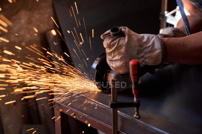 Обрезанное изображение рабочего в защитных очках и перчатках, режущих металл молотилкой с летящими искрами во время работы в мастерской — стоковое фото