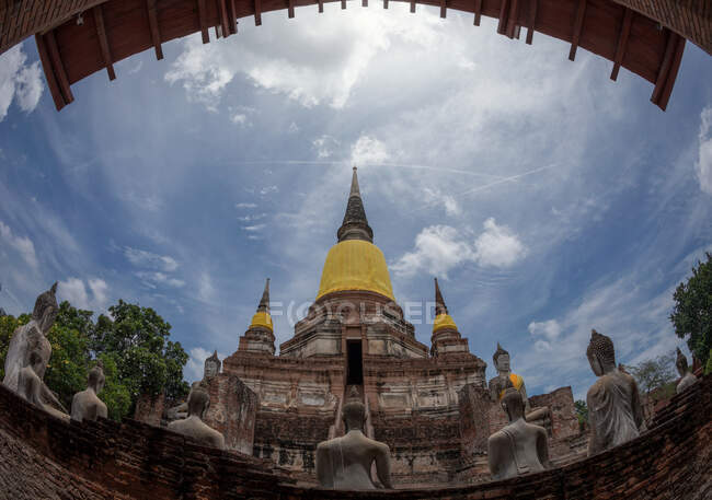 Dal basso antico tempio buddista con statue in cortile contro cielo nuvoloso nella giornata di sole in Thailandia — Foto stock