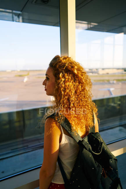 Задній вид кучерявої жінки з рюкзаком спостереження поля з літаками в аеропорту Техасу. — стокове фото