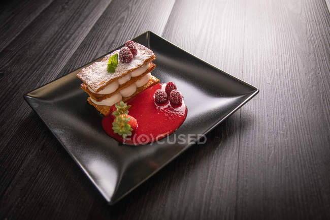 De arriba la crema dulce gourmet Diphlomate y la cedadela de frutas rojas en el plato negro cuadrado en fondo gris. - foto de stock