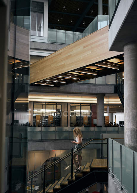 Vista lateral de mujer casual bajando escaleras en edificio de biblioteca contemporánea en Texas - foto de stock