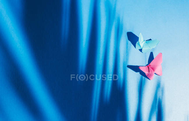 Mariposas frágiles hechas de papel con sombra de hoja de palmera adosada a la tela de seda azul. - foto de stock