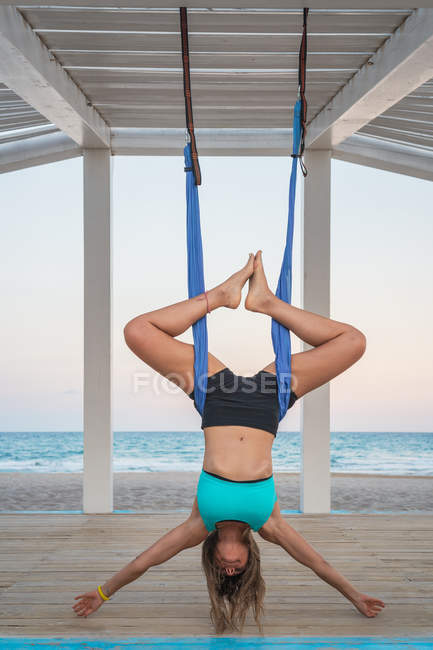 Mujer relajada realizando yoga aéreo colgando cabeza abajo - foto de stock