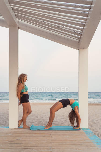 Partner looking at woman making bridge in acroyoga on background of ocean — Stock Photo