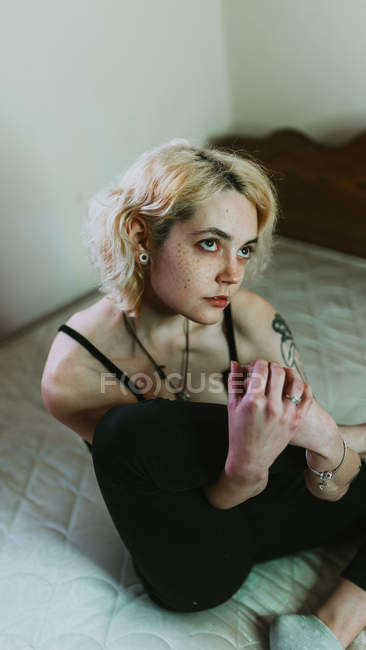 Mujer joven atenta y pensativa sentada en la cama y mirando hacia otro lado - foto de stock