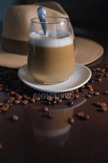 Glass of hot drink in composition with hat and coffee grains on wooden table — Stock Photo