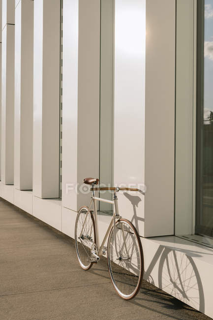 Велосипед припаркован на тротуаре возле стены современного здания в солнечный день на городской улице — стоковое фото