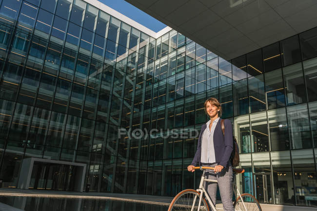 Seitenansicht einer entzückten Unternehmerin, die an einem sonnigen Tag in der Innenstadt der modernen Stadt lächelt und Fahrrad fährt — Stockfoto