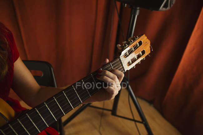 Mano de corte de mujer artística irreconocible en vestido rojo interpretando canción tocando en la guitarra en el escenario en España - foto de stock