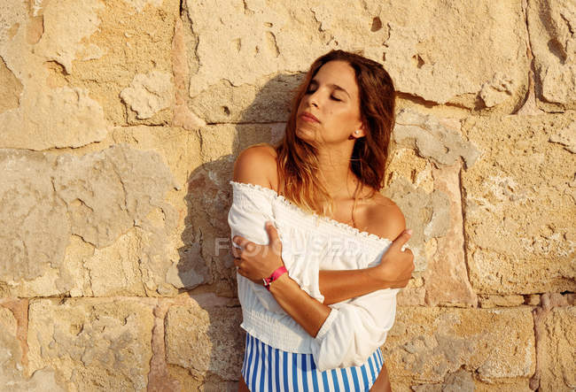Viajante em blusa branca desfrutando de férias enquanto está de pé e embrulhando-se em braços com parede balançada no fundo — Fotografia de Stock