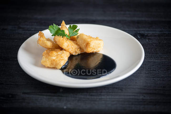 Fresh appetizing Hake breaded with squid cream in white plate on gray background — Stock Photo