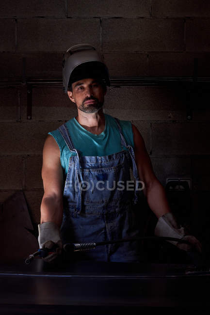 Профессиональный человек в маске на голове в джинсах и защитных перчатках, стоящих на рабочем месте — стоковое фото