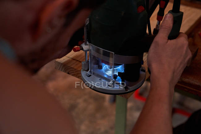 Immagine ritagliata dell'uomo utilizzando fresatrice per la lavorazione di tavole di legno mentre si lavora sul posto di lavoro — Foto stock