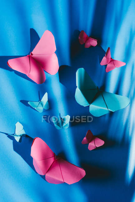 Крихкі метелики з паперу з тінню пальмового листя прикріплені до синьої шовкової тканини. — стокове фото