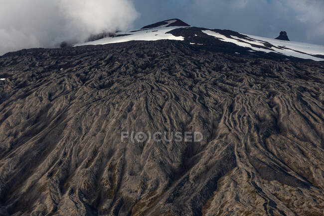 Снизу грубый склон и снежная вершина горы против облачного неба в Исландии — стоковое фото