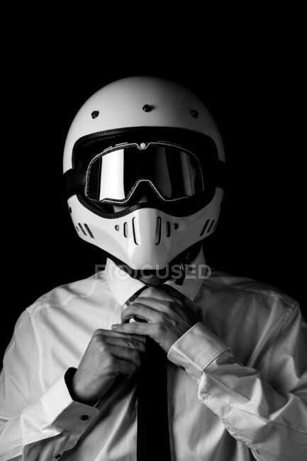 Black and white of anonymous racer in formal white and tie wearing modern shiny helmet with black goggles in studio — Stock Photo