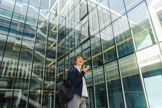 Low angle of happy businesswoman holding hand in pocket and using smartphone while standing outside business center on city street — Stock Photo