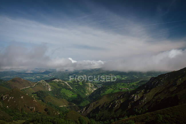 Perspective amazing view of green hills with dense forest and meadows under thick lush clouds in Asturias in sunny day — Stock Photo