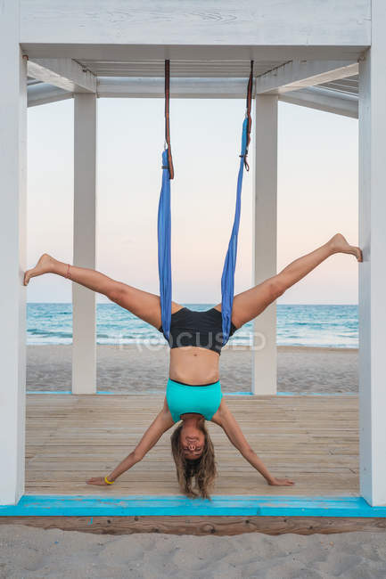 Mujer relajada realizando yoga aéreo colgando cabeza abajo - foto de stock