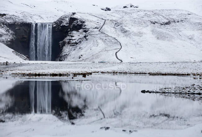 Kaltes sauberes Wasser fällt von einem schneebedeckten Hügel in der Nähe eines ruhigen Sees in der Natur in Island — Stockfoto