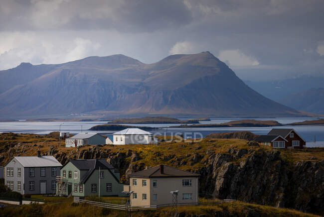 Прекрасные дома, расположенные на берегу моря возле горного хребта в облачный день в Исландии — стоковое фото