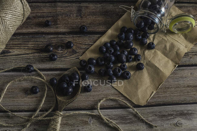 Top view of shiny jar with scattered fresh blueberries on hardwood table decorated with wooden spoon and twine — Stock Photo
