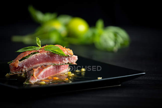 Fragrante tonno rosso succoso con prosciutto di basilico e demiglace di pollo su piatto nero — Foto stock