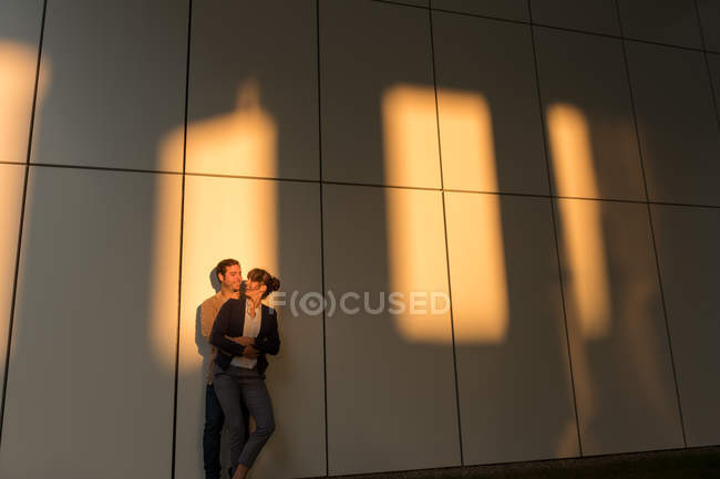 Empresario abrazando y besando a su novia mientras está parado fuera del edificio moderno después del trabajo - foto de stock