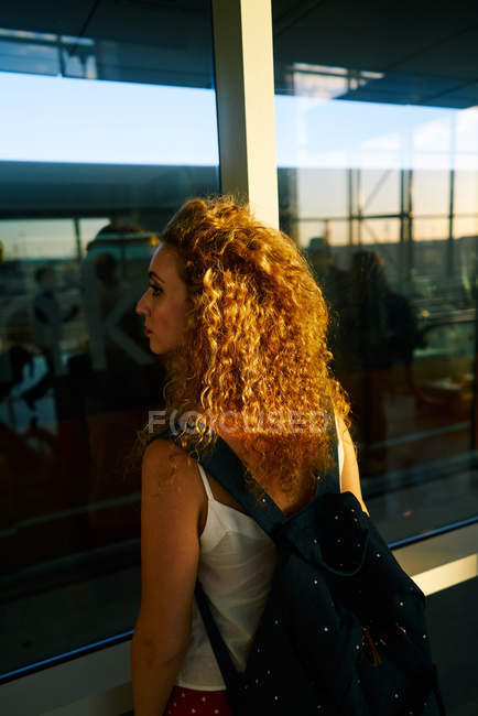Вид сзади кудрявая стильная женщина с рюкзаком наблюдая поле с самолетами в аэропорту Техаса — стоковое фото