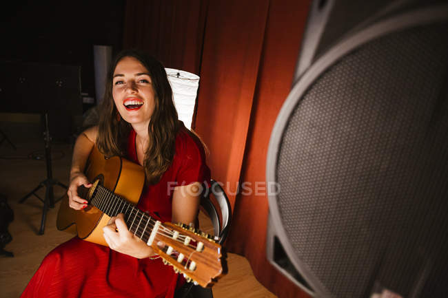 Приваблива художниця в червоному вбранні грає пісню на гітарі на сцені з теплим світлом в Іспанії. — стокове фото