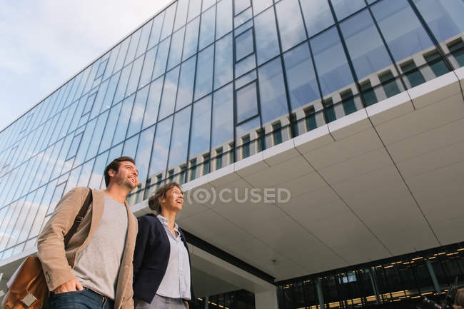 Von unten glückliche Paar-Kollegen Händchen haltend in lässigen Outfits lächelnd und gemeinsam vor dem modernen Gebäude auf der Stadtstraße nach der Arbeit — Stockfoto