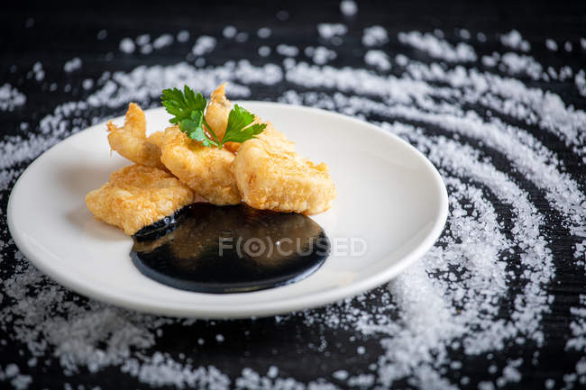 Merluza empanada con crema de calamar en plato - foto de stock