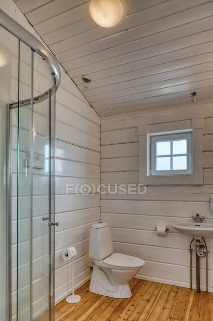 Elegante interior do banheiro minimalista com piso de madeira e paredes brancas com pequena janela em casa — Fotografia de Stock